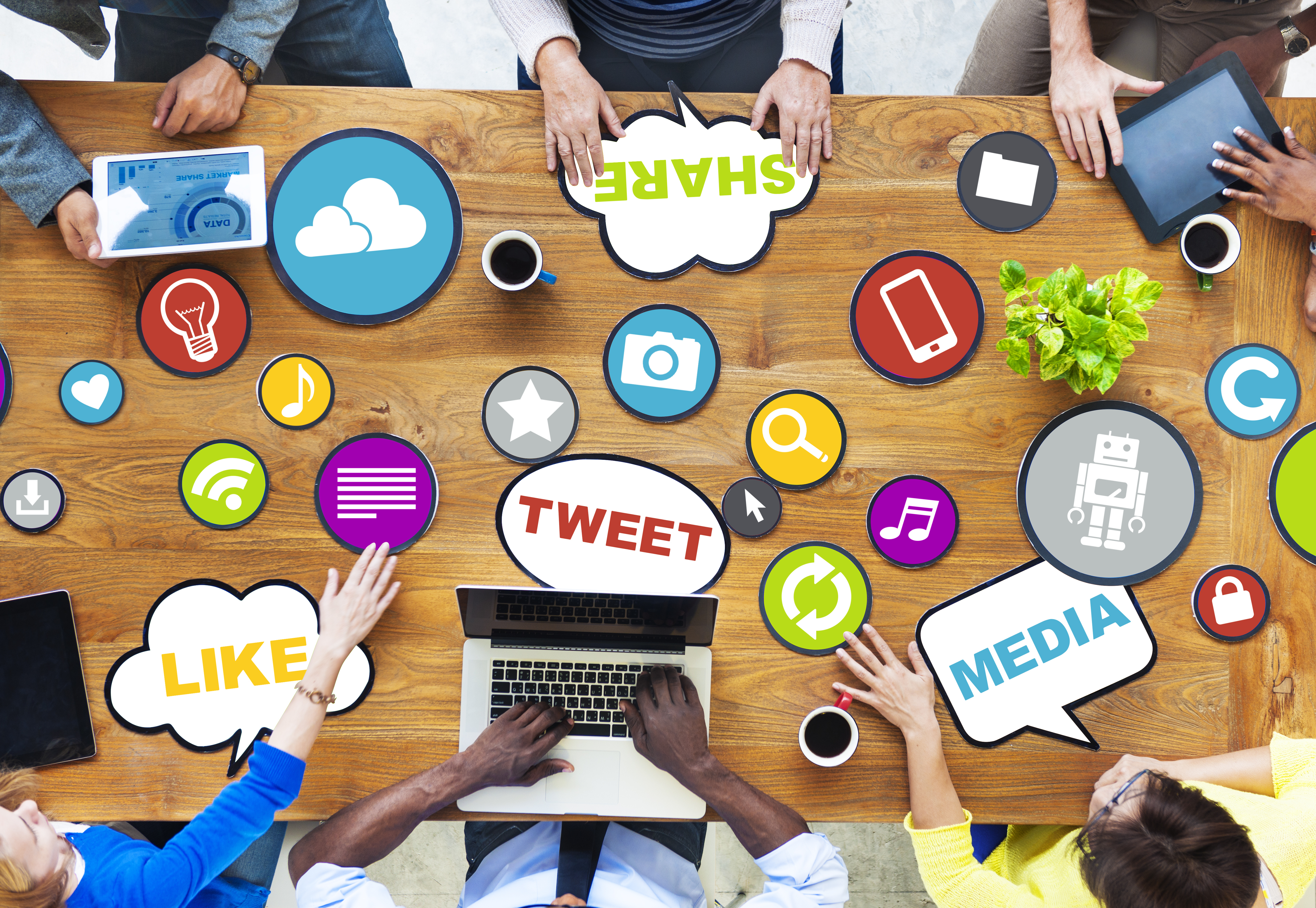 Group of people working on their devices at the table. The table is covered with words and icons related to social media.